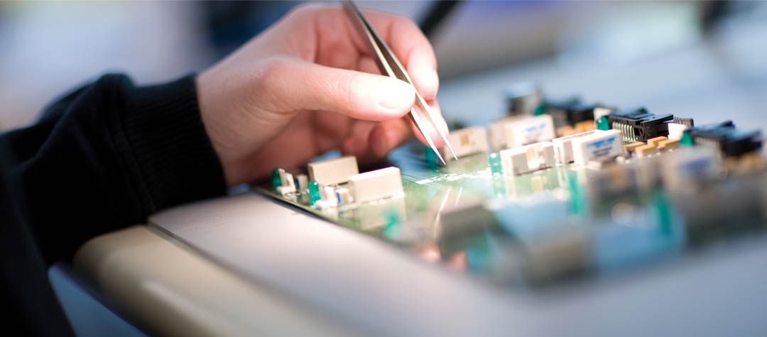 A person's hand working with a circuit board.
